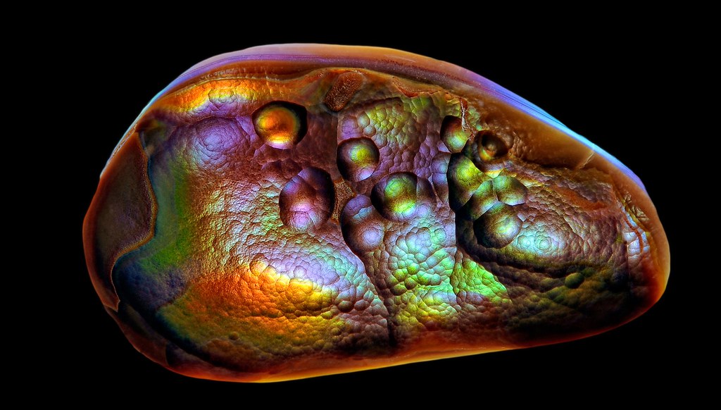 Ágata de fogo iridescente com formações em bolhas, sobre fundo preto