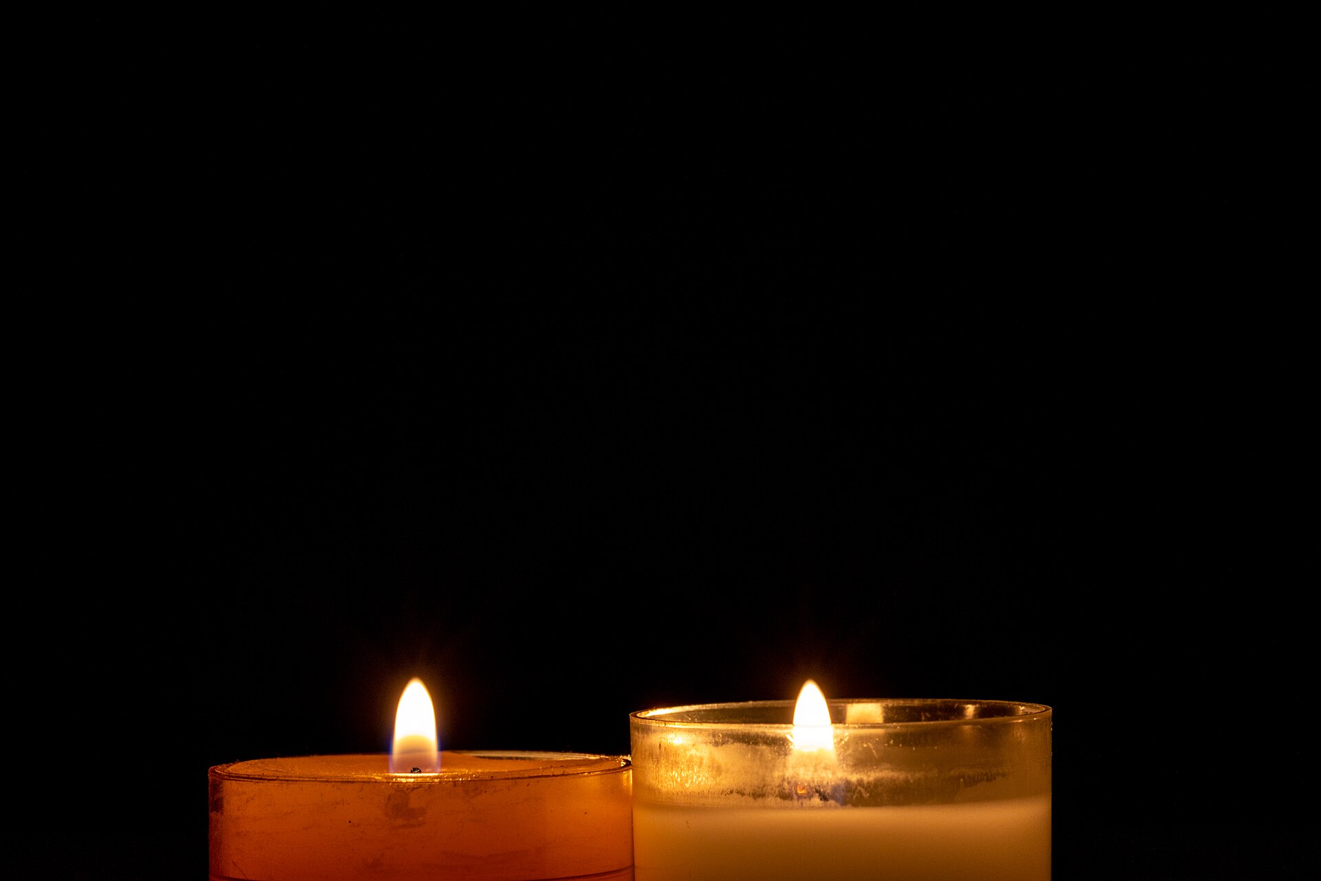Duas velas acesas lado a lado sobre fundo escuro, cada uma com sua própria chama
