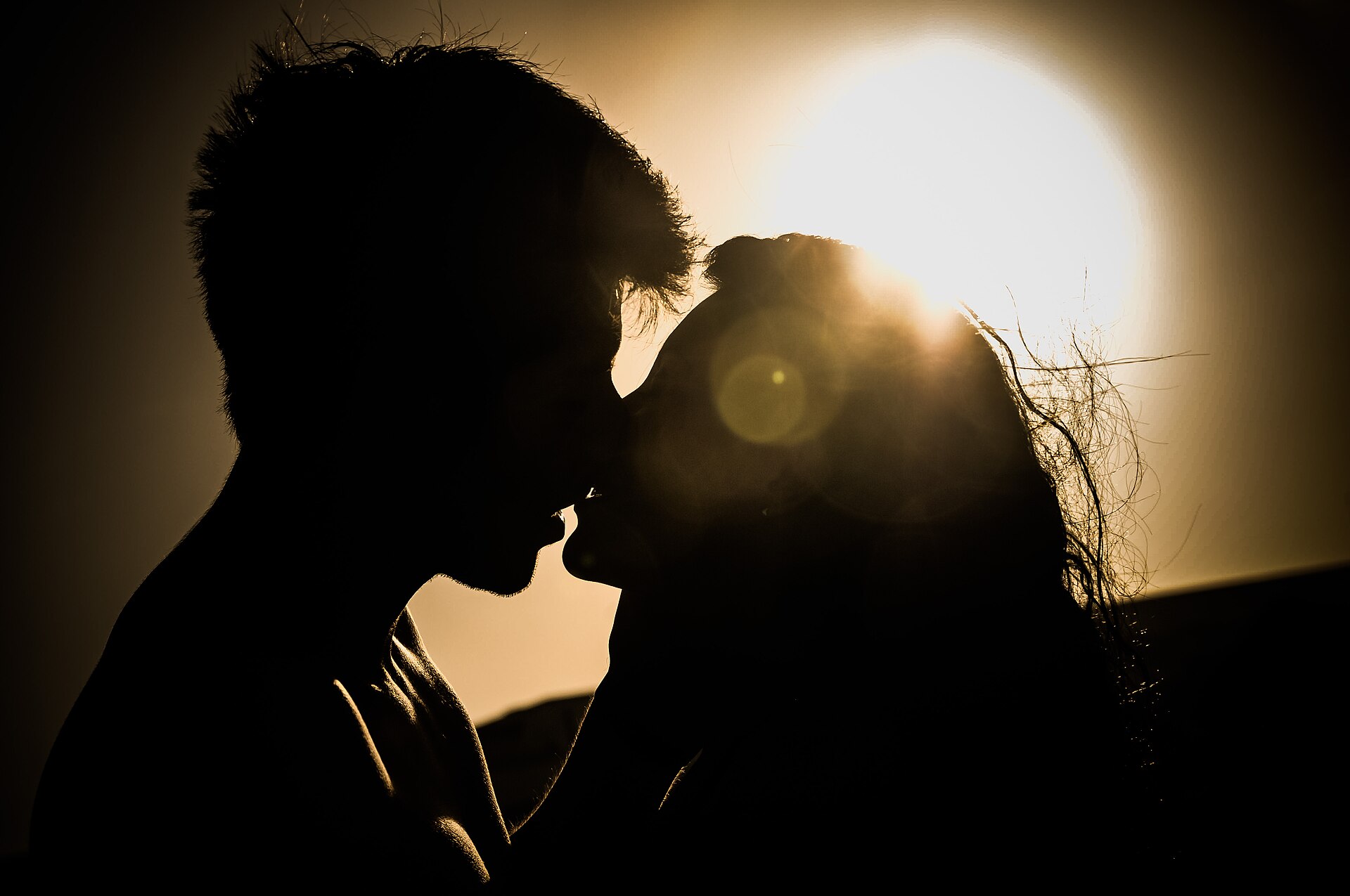 Silhueta de duas pessoas se beijando contra a luz do pôr do sol