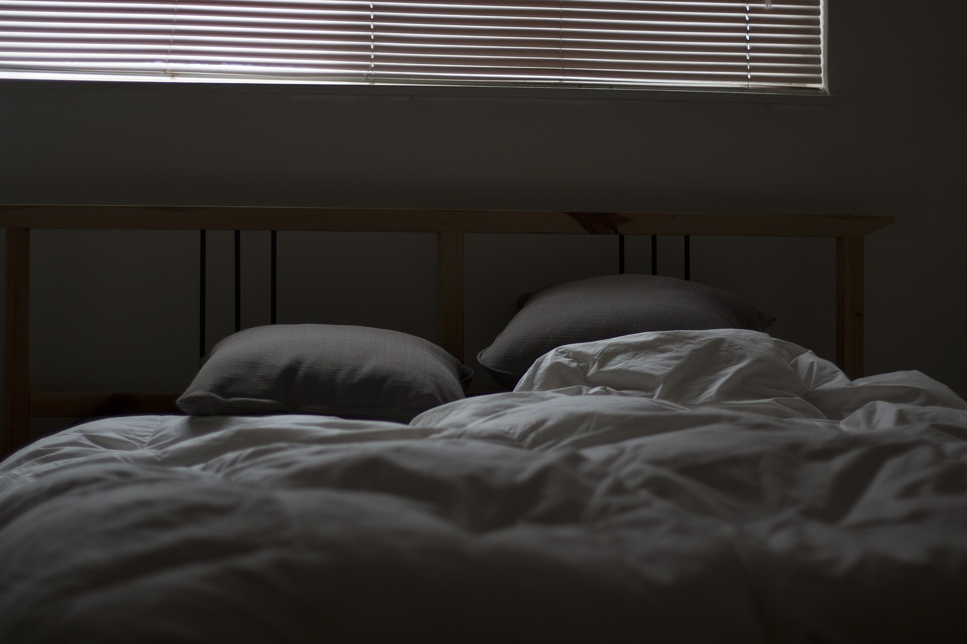 Cama desarrumada em quarto escuro, com luz entrando pela persiana ao amanhecer